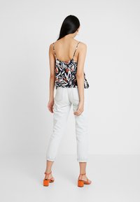 Bagud udsigt af en mønstret, ærmeløs top med tynde stropper, prydet med et navy, hvidt og rødt design, parret med lyse denim og orange hæle.