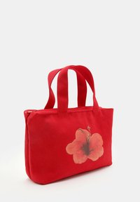 Červená plátěná taška s dvěma krátkými ušima, na jedné straně s velkým potiskem květu hibisku. Zapínání na zip, pevná textura.