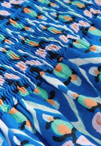 Blått tyg med en texturerad, rynkad design. Har ett färgglatt blommönster i grönt, rosa och svart som förhöjer det estetiska.