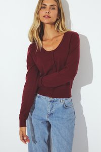 Burgundy cardigan with a scoop neckline, front buttons, and long sleeves. Paired with light blue high-waisted denim jeans.