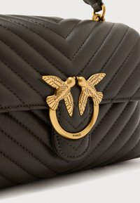 Πλεκτή τσάντα χειρός από σκούρο πράσινο δέρμα με κούμπωμα διακοσμημένο με χρυσό πουλί και κυκλικό μεταλλικό στοιχείο, διαθέτει διαγώνιες ραφές και ομαλή υφή.