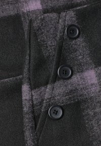 Tissu en laine gris foncé avec un motif à carreaux violet discret, comportant trois boutons noirs à quatre trous cousus sur un manteau ou une veste.