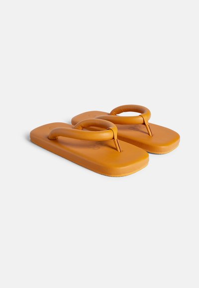 Oranje rubberen flip-flops met brede zolen en ronde banden. De banden hebben een gladde textuur en een subtiel logo dat op de voetbed is gedrukt.