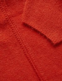 Roter Strickstoff mit weicher Textur, der eine sichtbare Naht und einen umgeschlagenen Bund aufweist. Die Fasern sind dezent flauschig, was auf Wärme und Komfort hinweist.