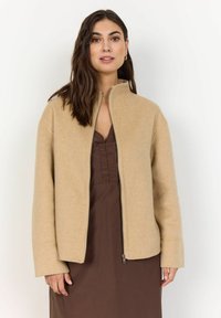 Beige gyapjúkeverék dzseki magas gallérral, elülső cipzárral és hosszú ujjakkal. Puha tapintású, enyhén bő szabású, barna ruhával párosítva.