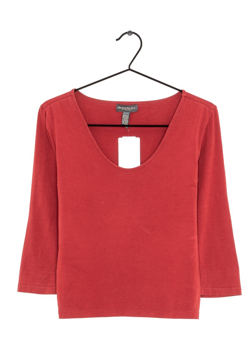 Červený top s dlouhým rukávem a hlubokým výstřihem ve tvaru V, vyrobený z měkkého materiálu. Obsahuje štítek visící z výstřihu. Jednoduchý design bez vzorů.