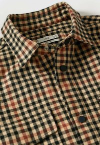 Chemise en flanelle à carreaux marron, noir et beige avec col, boutons et poche poitrine. Texture douce avec une coupe régulière.