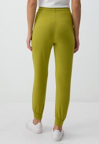 Grüne Jogginghosen aus weichem Material, mit einem engen Knöchelbund und einem elastischen Taillenbund für zusätzlichen Komfort. Kombiniere sie mit weißen Sneakers.
