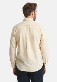 Maglietta a maniche lunghe a righe gialle e bianche con colletto classico, polsini con bottoni e piega sul retro. Tessuto di cotone liscio.