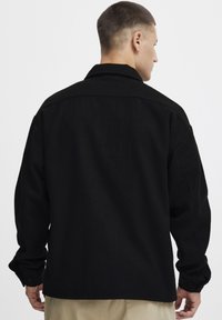 Black wool blend shirt jacket with a casual design, long sleeves, and button cuffs. Features a pointed collar and a relaxed fit.