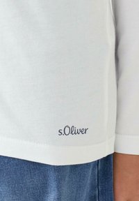 Jasny bawełniany t-shirt z podwiniętymi rękawami, prostym krojem i haftowanym logo "s.Oliver" w pobliżu dolnego brzegu.