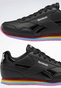 Baskets Reebok noires avec des bandes arc-en-ciel sur la semelle intermédiaire et une semelle extérieure rose, avec des lacets noirs et le logo blanc Reebok sur les côtés et la languette.