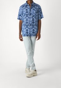 Modrá krátká košile s vířivým vzorem, design na knoflíky, kapsa na levé straně, spárovaná s světle modrými džíny a béžovými teniskami.