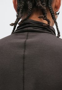 Donkerbruine trui met een hoge kraag en een centrale naad aan de achterkant. De stof lijkt glad en heeft een zachte textuur.