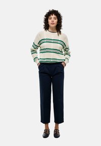 Pull en maille épais crème avec des rayures vertes, associé à un pantalon taille haute bleu marine et des chaussures noires à boucles.