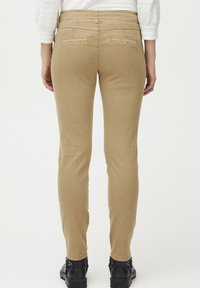 Pantalones vaqueros ajustados color beige con una textura suave, de cintura media y dos bolsillos traseros. Combinados con botas negras hasta el tobillo.