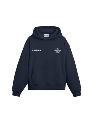 Person with curly blond hair wearing a navy hoodie with yellow text reading "Don't forget to: Chill Out On Vacation Club" on the back.