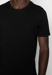 Black cotton t-shirt with short sleeves, round neckline, and a smooth texture. Features a simple, unembellished design with no patterns.