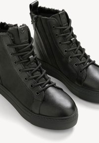 Black high-top shoes made of textured leather, featuring a lace-up front, side zipper, and a soft fur lining around the collar.