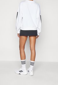 Vit oversized sweatshirt med svarta detaljer, kombinerad med en mörkgrå kjol. Vita sneakers och randiga svartvita strumpor fulländar looken.