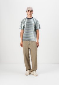 Stribede bomulds t-shirt med korte ærmer, marineblå krave, lille emblem på brystet, parret med beige løstsiddende bukser og lyse sneakers.