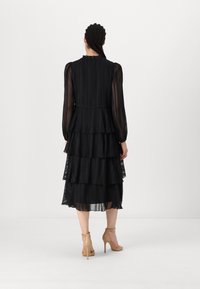 Black tiered dress with sheer material, long sleeves, ruffled neckline, and a layered skirt. Worn with nude high-heeled shoes.