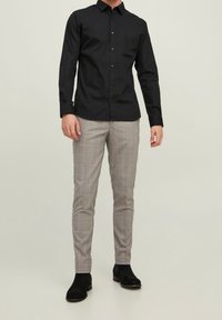 Camicia nera con bottoni e maniche lunghe abbinata a pantaloni grigi a quadri. I pantaloni presentano un delicato motivo a scacchi e una vestibilità slim. Stivaletti neri alla caviglia.
