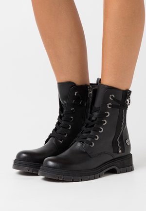 Bottes courtes en cuir noir avec lacets à l'avant, fermeture éclair latérale et semelle en caoutchouc texturée. Équipées de ferrures argentées et d'un accent floral.