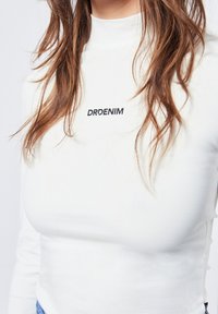 Weißes Langarmshirt mit hohem Kragen und schwarzem "DRDENIM"-Logo auf der Brust. Glatte Textur mit taillierter Passform.