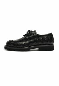 Scarpa in pelle nera con lacci e motivo intrecciato, suola in gomma spessa e punta arrotondata, mostrata in profilo laterale su sfondo bianco.
