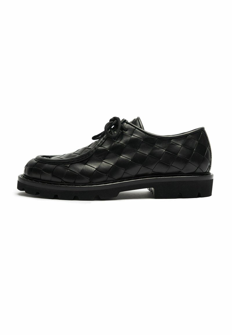 Scarpa in pelle nera con lacci e motivo intrecciato, suola in gomma spessa e punta arrotondata, mostrata in profilo laterale su sfondo bianco.