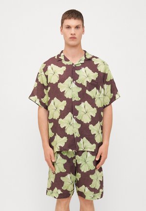 Hawaiian-style outfit featuring a short-sleeve shirt and shorts in a brown fabric with large green leaf patterns and white accents.