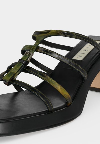 Μαύρο σανδάλι με τακούνι με λεπτά ελαιί πράσινα και μαύρα λουράκια και μικρή ασημένια αγκράφα, με τετράγωνη μύτη και μαξιλαρωμένο πάτο.