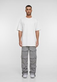 Tricou alb supradimensionat cu mâneci scurte, asortat cu pantaloni cargo gri cu multiple buzunare și adidași gri. Design simplu.