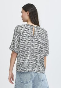 T-shirt à manches courtes avec un motif géométrique noir et blanc, en tissu doux, avec un détail en trou de serrure à l'arrière, associé à un short en jean.