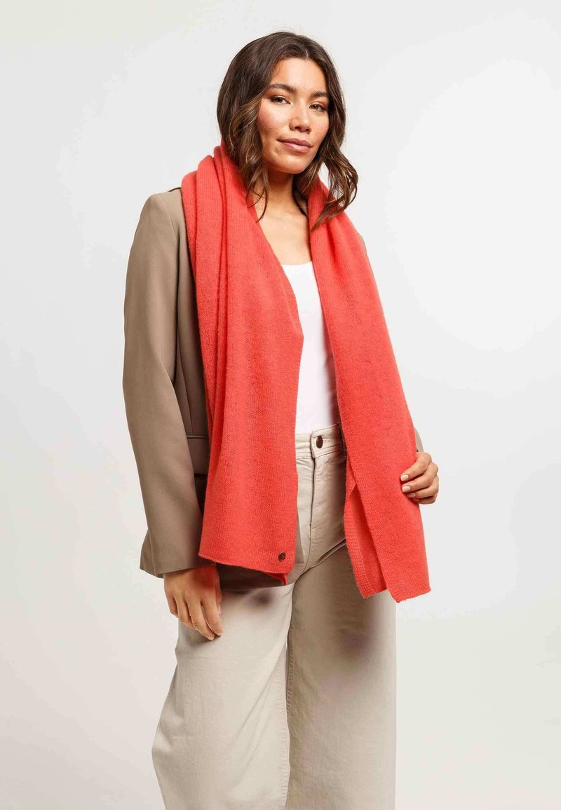 Foulard corallo realizzato in materiale morbido, drappeggiato attorno al collo. Presenta una superficie liscia con una leggera lucentezza e un dettaglio con bottone.