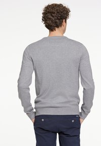 Grå stickad tröja med långa ärmar, rund halsringning och ribbade muddar, kombinerad med marinblå byxor med två knappförsedda bakfickor.