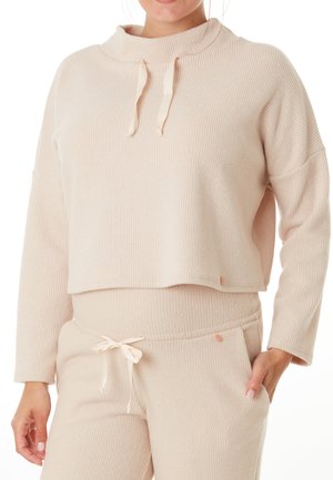 Pull en beige clair côtelé avec un col haut, des cordons de serrage et des manches larges, associé à un pantalon côtelé assorti avec un lien à cordon.