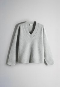 Světle šedý svetr s výstřihem do V, dlouhými rukávy a žebrovanými manžetami, lemem a výstřihem, zobrazený na jednoduchém světlém pozadí.