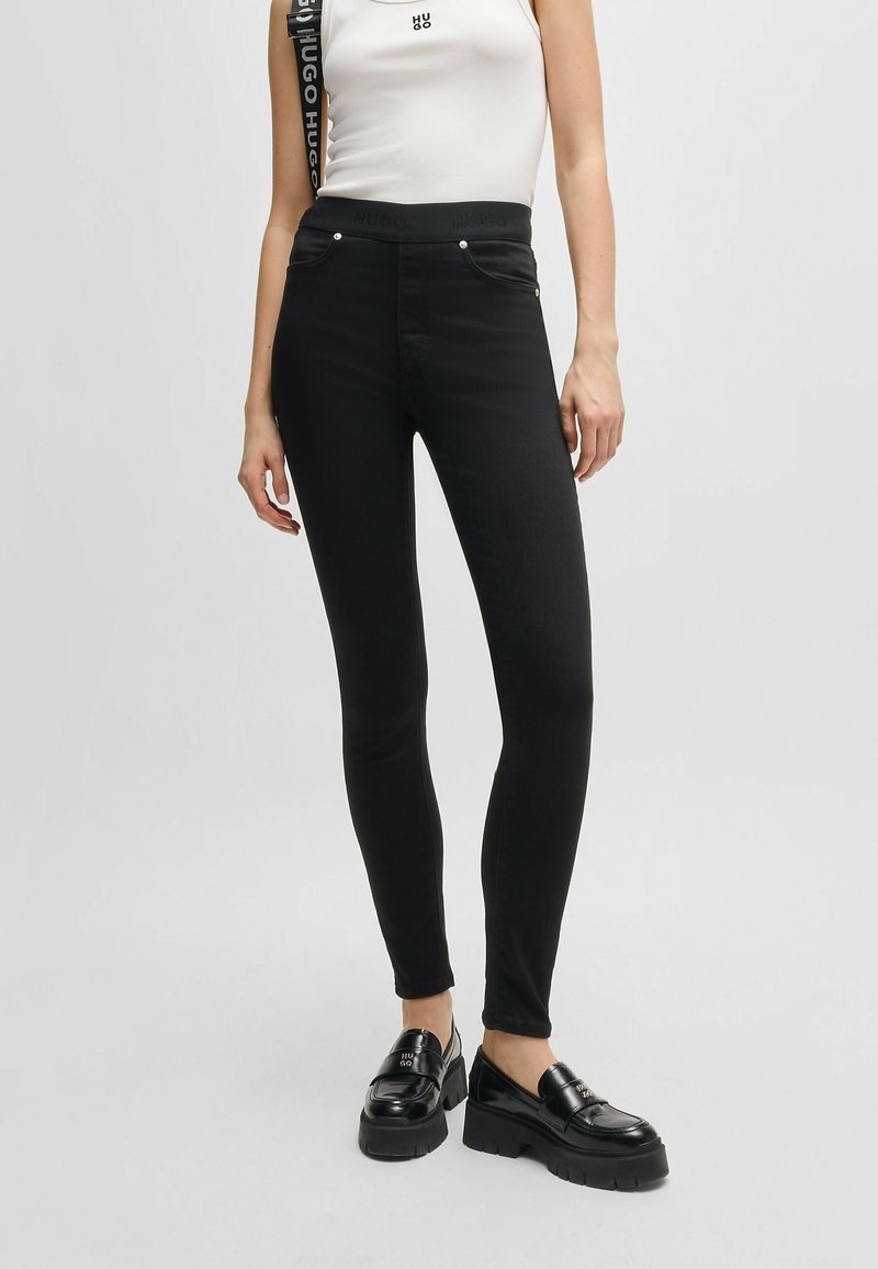 Jeans skinny neri in denim con vita alta, design a cinque tasche e dettagli metallici argento, abbinati a mocassini neri voluminosi.