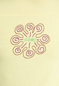 Rumena tkanina s osrednjim vezenim motivom, obdanim z rjavimi in vijoličnimi spiralami, ki obkrožajo zeleni besedi "ubogaj." Vodoodporna tekstura.