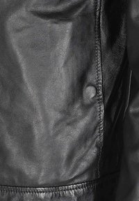 Sort læderjakke med en struktureret overflade, synlige stikninger og en trykknaplukning på siden. Glat og tætsiddende design.