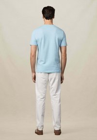 T-shirt bleu clair à manches courtes, col ras du cou, associé à un pantalon blanc. La tenue présente une coupe décontractée et une texture en coton lisse.