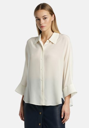 Light cream button-up blouse with a collar, three-quarter sleeves, and a smooth, flowing fabric. Features a relaxed fit and a rounded hem.