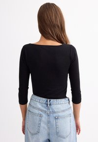 Top negro de manga larga con escote redondeado, combinado con jeans de mezclilla azul claro de cintura alta que presentan dos bolsillos traseros.