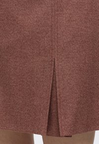 Gros plan d'une jupe marron texturée avec une fente centrale au dos montrant une petite portion des jambes de la porteuse sous l'ourlet.