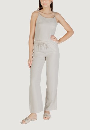 Jumpsuit beige chiaro con spalline sottili, vita elastica e gambe larghe, realizzato in tessuto morbido. Indossato con sandali chiari.