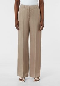Szerokie spodnie w jasnobeżowym kolorze, wykonane z gładkiego materiału, z dopasowanym pasem i plisowanym przodem. W połączeniu z białymi sandałami na paski.