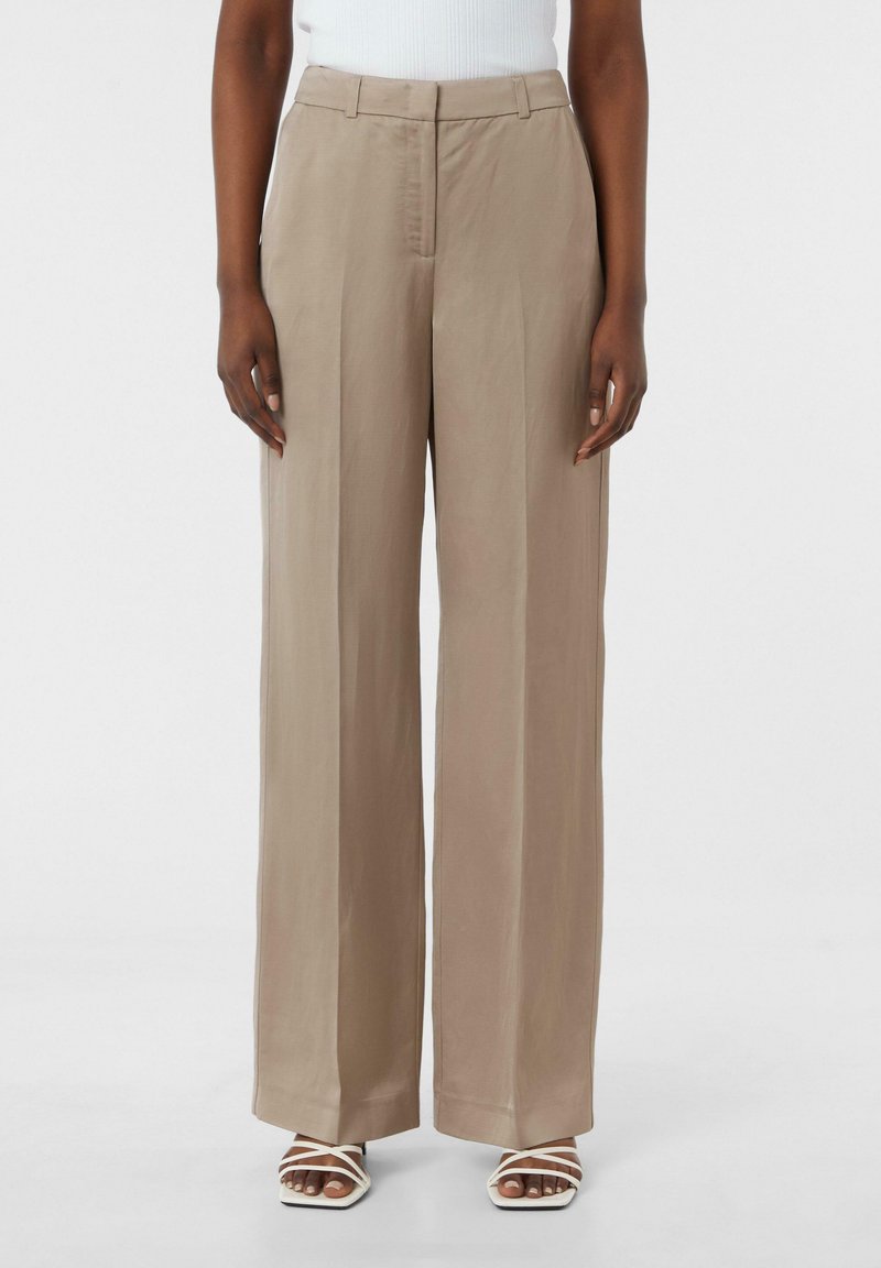 Szerokie spodnie w jasnobeżowym kolorze, wykonane z gładkiego materiału, z dopasowanym pasem i plisowanym przodem. W połączeniu z białymi sandałami na paski.