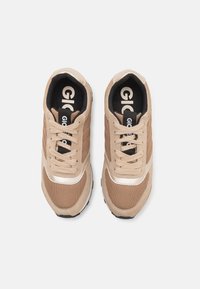 Beige treningssko laget av mesh og semsket skinn. Har en hvit stripe, svarte såler og en svart innside med logo. Snøring inkludert.